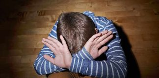 A child sitting on the floor with their hands covering their face expressing distress
