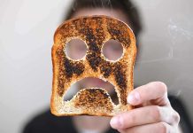 A person holding a slice of burnt toast shaped like a sad face