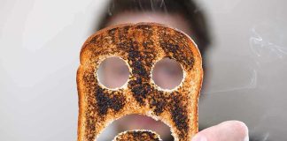 A person holding a slice of burnt toast shaped like a sad face