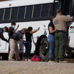 Border patrol officers investigating people near a bus.