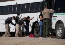 Border patrol officers investigating people near a bus.