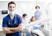 A dentist smiling in a dental office with a team assisting a patient