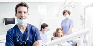 A dentist smiling in a dental office with a team assisting a patient