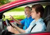 A young man driving a car with an older man giving instructions