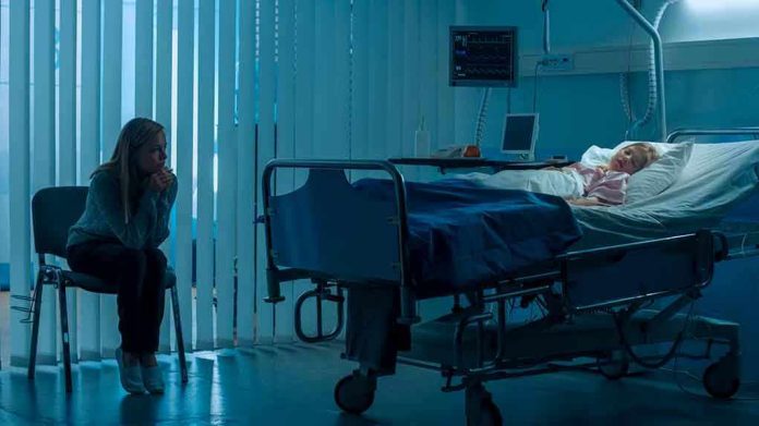 Woman sitting beside hospital bed at night.