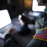 Top General’s Blast Safety Move Stuns Pentagon Soldier using laptop with US flag patch visible.