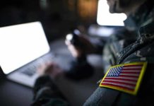 Top General’s Blast Safety Move Stuns Pentagon Soldier using laptop with US flag patch visible.