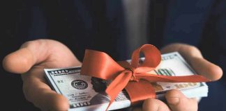 Hands holding stack of hundred-dollar bills with ribbon.