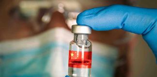 Gloved hand holding vial with red liquid and flag.