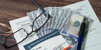 Medicare card glasses pen money on wooden table