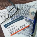 Terrifying Hospital Bills EXPOSED By Trump Move Medicare card glasses pen money on wooden table