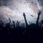 Crowd celebrating under confetti and bright lights.