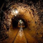 Dimly lit underground tunnel with rail tracks and rocky walls
