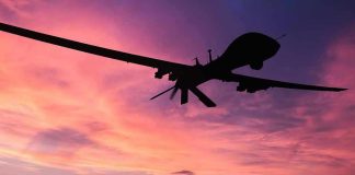 Navy Unleashes Drone Fleet Onslaught Silhouette of a drone against a colorful sunset.
