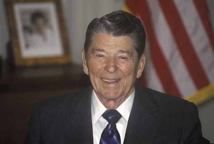 A smiling man in a suit with an American flag in the background