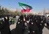 Group of women in black attire marching with an Iranian flag