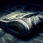 A rolled stack of hundred-dollar bills on a background of more banknotes