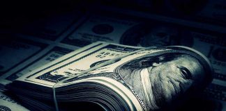 A rolled stack of hundred-dollar bills on a background of more banknotes