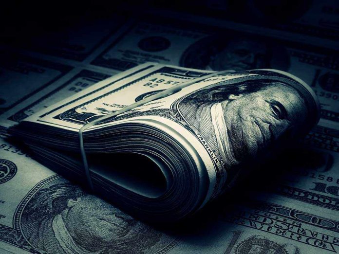 A rolled stack of hundred-dollar bills on a background of more banknotes