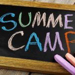 Chalkboard with colorful writing that says Summer Camp and several pieces of chalk