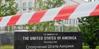 U.S. Embassy sign behind red-and-white caution tape.