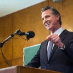 Newsom’s Law Opens Door to Huge Local Pay Hikes A man in a suit delivering a speech at a podium with microphones