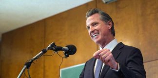Newsom’s Law Opens Door to Huge Local Pay Hikes A man in a suit delivering a speech at a podium with microphones
