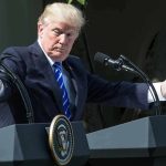 man at podiums with arms outstretched during outdoor press event