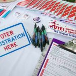 Voter registration table with forms, pens, and informational materials