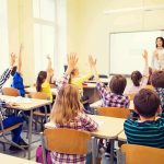 Students raise hands in a classroom with a teacher at the front