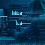 Hooded person at multiple computer screens with code and charts