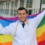 Smiling doctor holding a rainbow flag outdoors