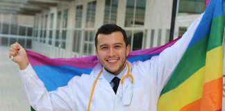 Smiling doctor holding a rainbow flag outdoors