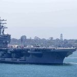 Aircraft carrier escorted by a tugboat in a harbor
