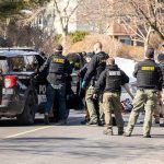 Police and sheriff officers gather around vehicles on a suburban street