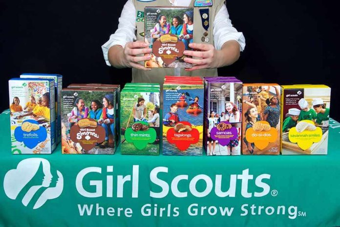 Girl Scout displays assorted cookie boxes on a table