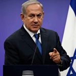man in suit speaking at a podium with an Israeli flag