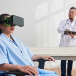Patient wearing VR headset sits as doctor observes with tablet