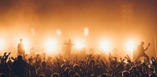 Rock band performing on stage with bright backlights and cheering crowd