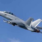 Twin-engine fighter jet climbing in a clear blue sky