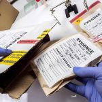 Gloved hands handling labeled evidence bags and boxes