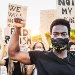 BLM DEMANDS Action After Floyd Joke on Netflix Protester wearing mask raises fist during demonstration