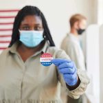 Voter wearing a mask holds an I Voted sticker at a polling place