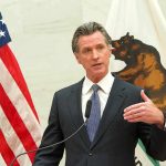 Gavin Newsom speaks at a podium with U.S. and California flags behind him