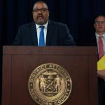 Why Luigi Mangione’s State Murder Trial Postponed Indefinitely Man speaks at podium with New York County District Attorney seal