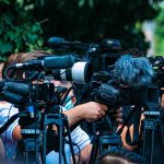 FDA Greenlights mRNA Flu Vaccine TV news cameras crowding together at an outdoor event