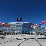 NATO headquarters with member flags in front under a clear blue sky