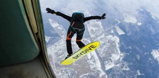 Skydiver jumps from plane with a skysurf board over snowy landscape