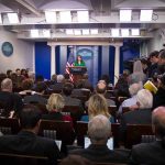 Press secretary at podium addressing reporters in briefing room