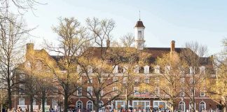 9 Universities Accused of REPLACING American Workers Students relaxing on a campus quad in front of a brick academic building